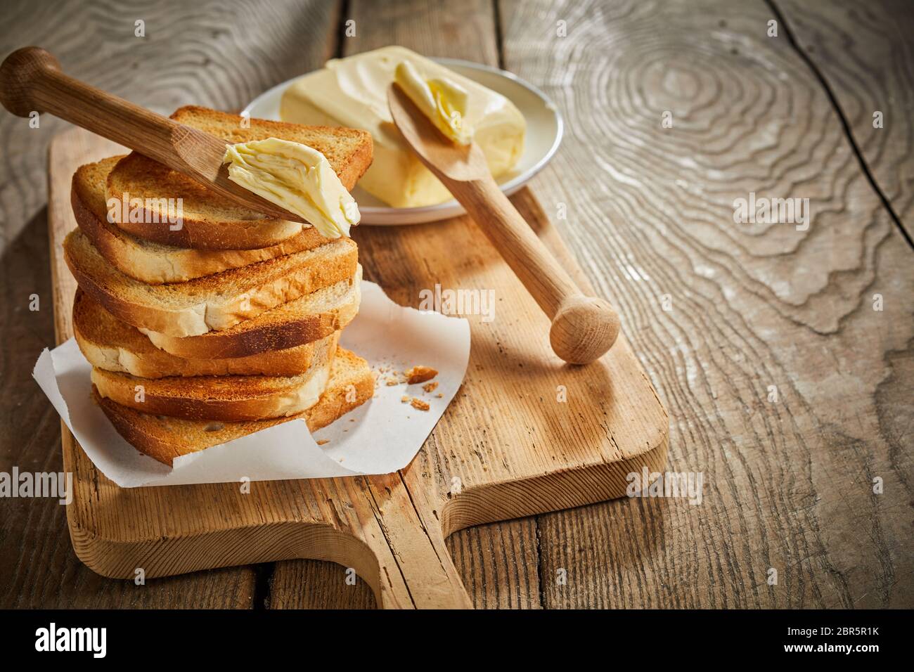 Freshly toasted white bread stacked on a board with a pat of farm ...