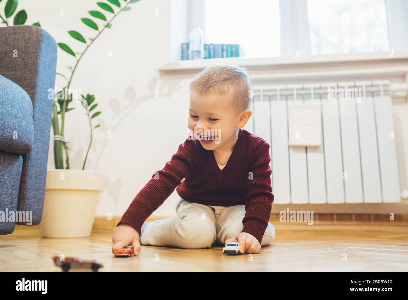 Lovely boy playing on the floor with some toy cars and laughing ...