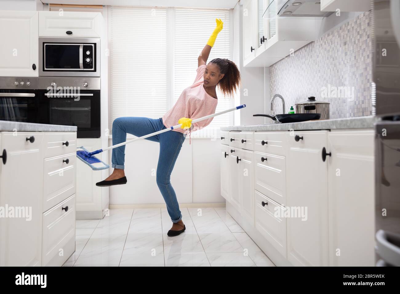 Close-up Of A Young African Woman Slipping While Mopping Floor In The Kitchen Stock Photo