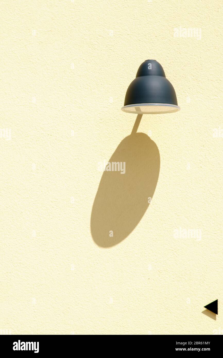 The close-up of a wall lamp and a small directional arrow casting a shadow on a plaster facade. Stock Photo