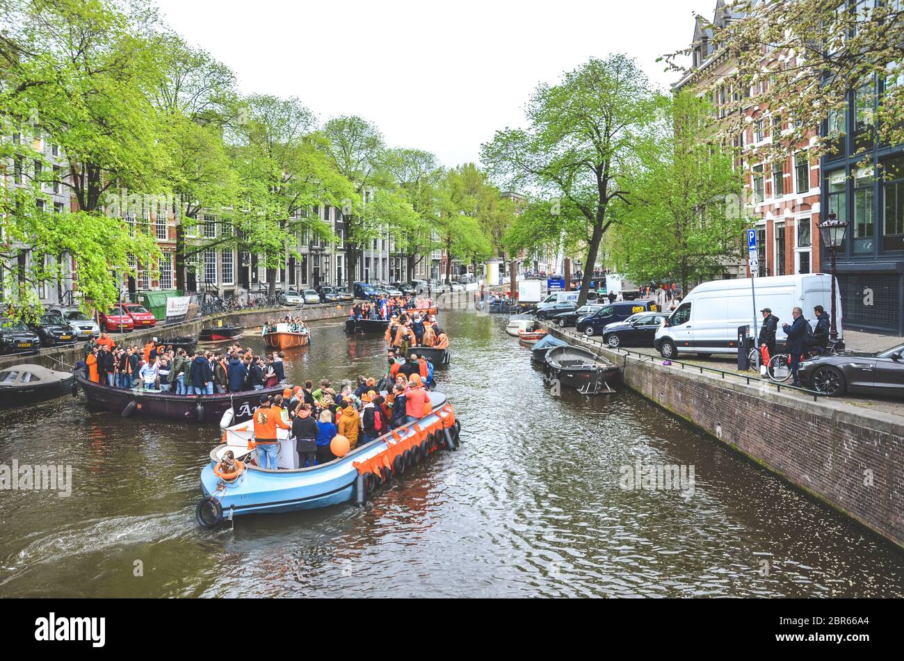 Amsterdam, Netherlands - April 27, 2019: Party boats with people dressed in national orange color while celebrating the Kings day, Koningsdag, the birthday of the Dutch King Willem-Alexander. Stock Photo