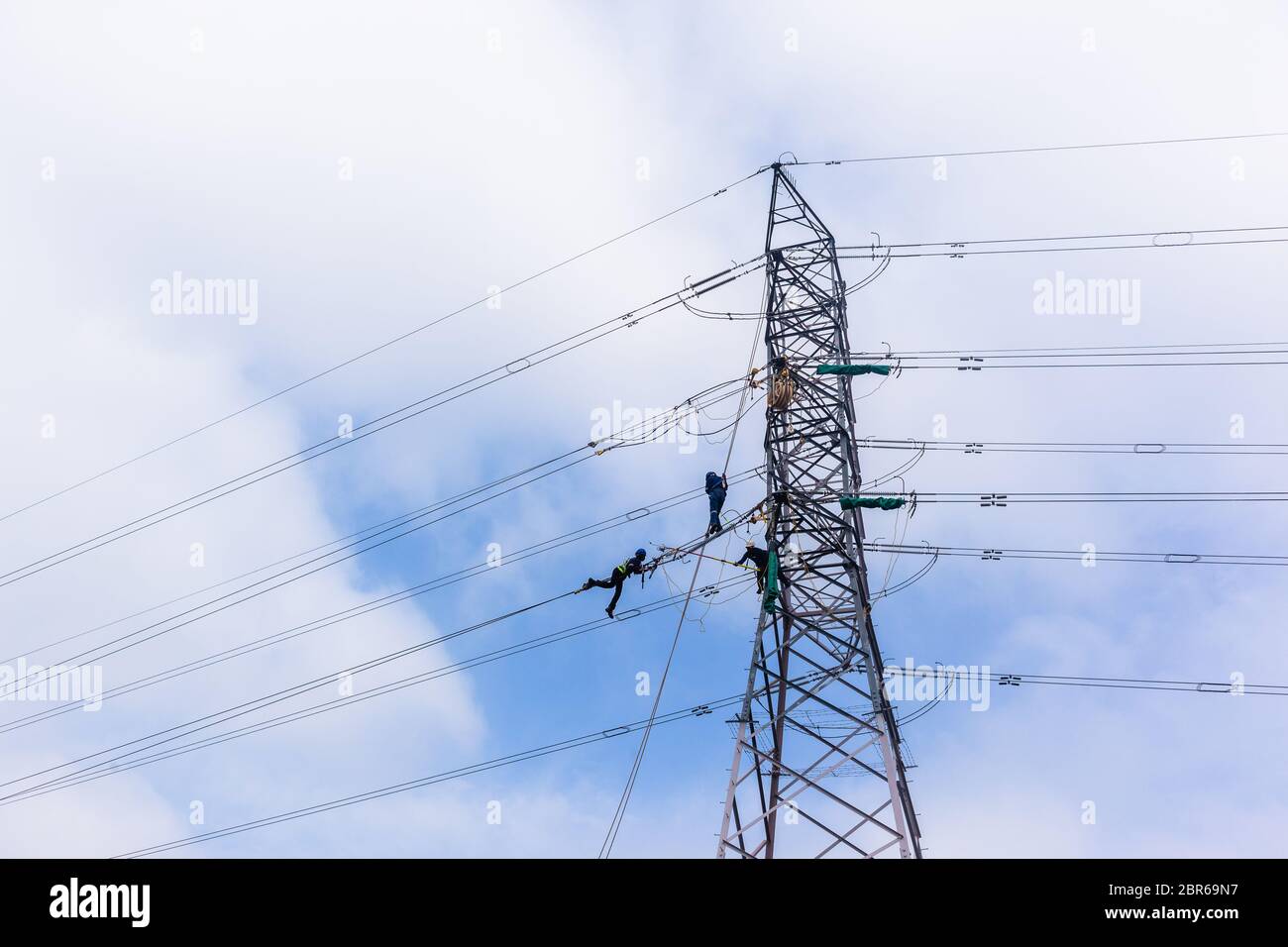 Electricians hanging on steel cables high above ground working on