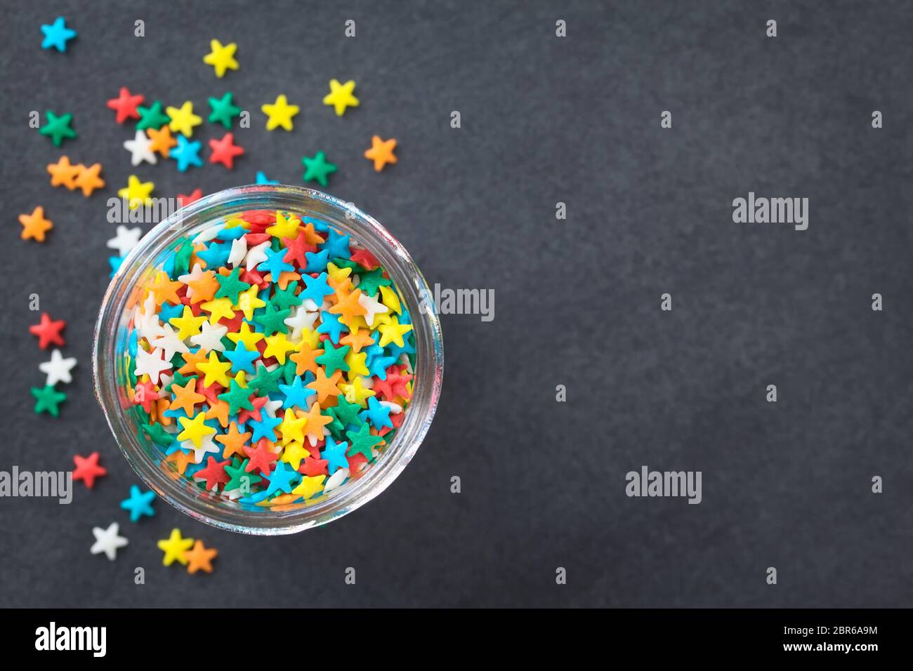 Colorful star shaped sugar sprinkles in glass jar, photographed overhead on slate (Selective Focus, Focus on the sprinkles in the jar) Stock Photo
