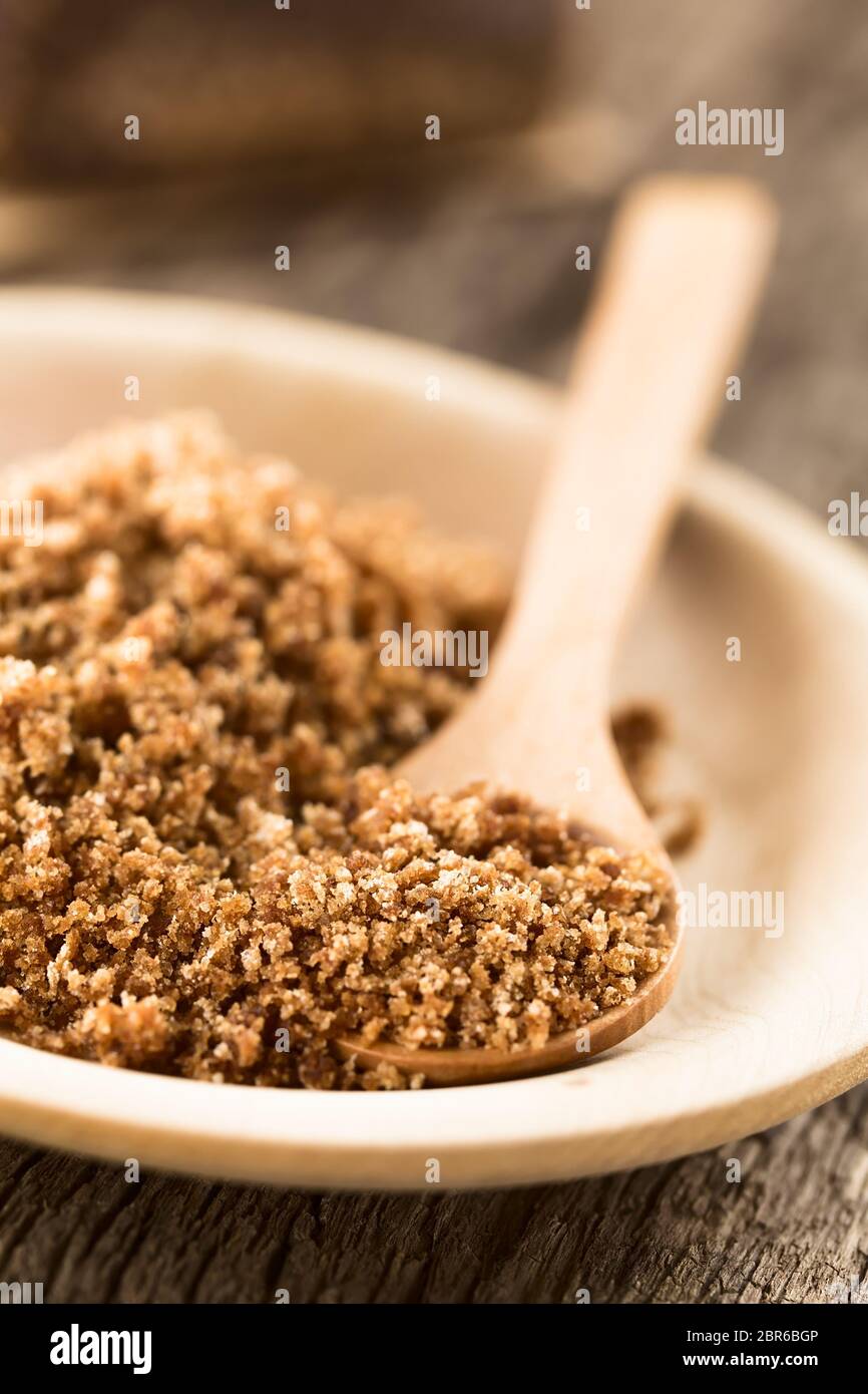 Grated panela or chancaca raw unrefined cane sugar on wooden plate with wooden spoon (Selective Focus, Focus one third into the image) Stock Photo