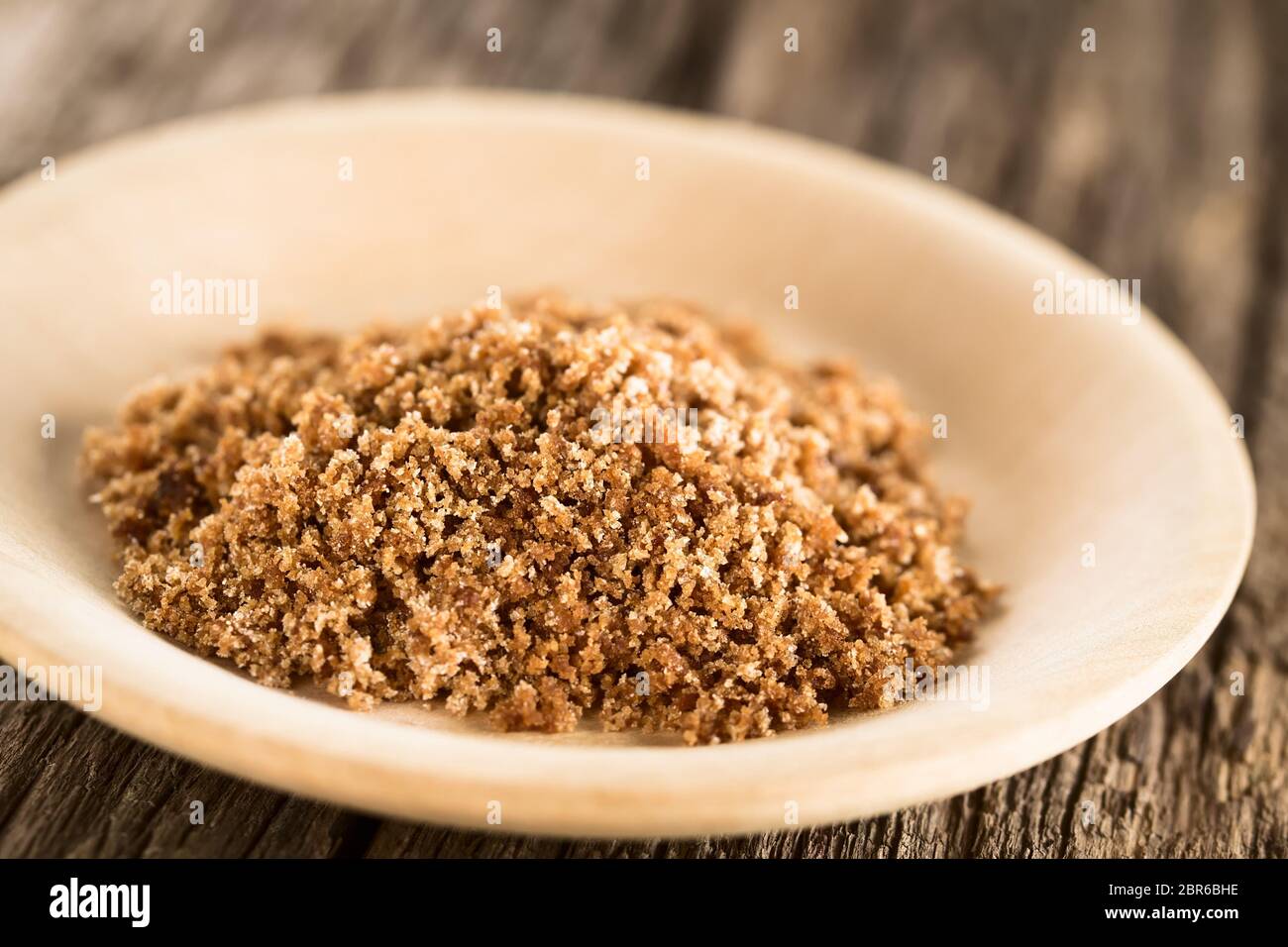 Grated panela or chancaca raw unrefined cane sugar on wooden plate (Selective Focus, Focus one third into the sugar) Stock Photo