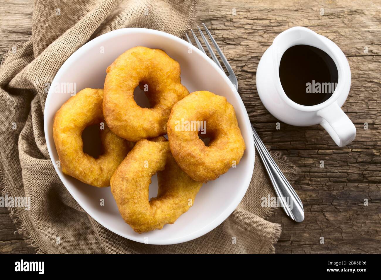 Traditional Chilean Picarones fried pastries made of pumpkin and flour yeast dough, served with sweet chancaca cane sugar sauce, photographed overhead Stock Photo