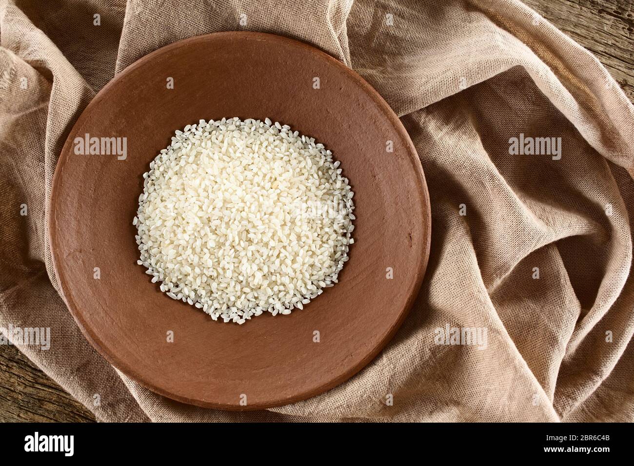 Raw arborio risotto shortgrain rice on clay plate, photographed