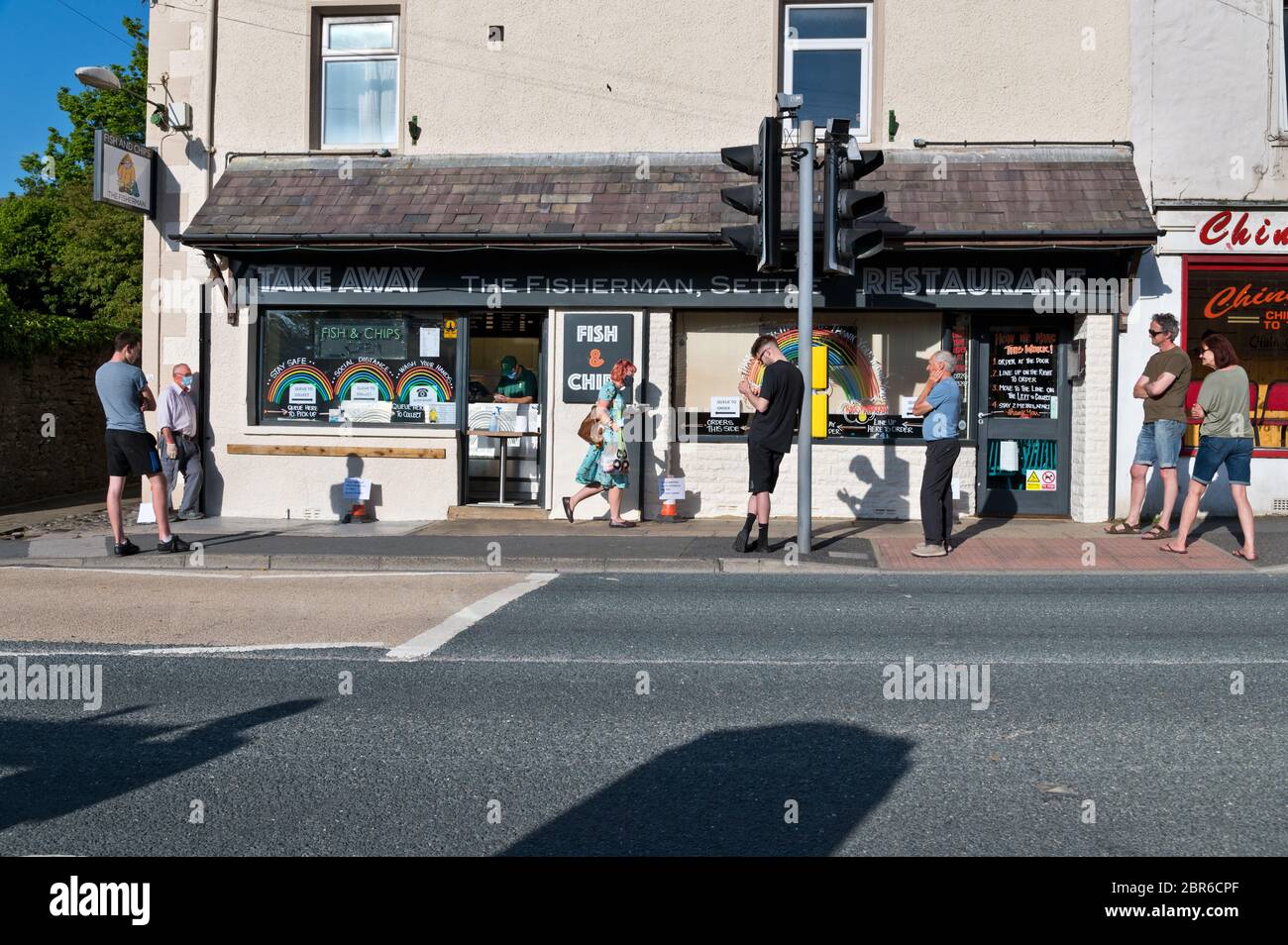 Settle, North Yorkshire, UK. 20th May 2020. Social distancing as people queue at a fish and chip shop, Settle, North Yorkshire, as a result of the Covid-19 restrictions. The instructions in the shop window say to queue on the right to order and then queue on the left to collect. Credit: John Bentley/Alamy Live News Stock Photo
