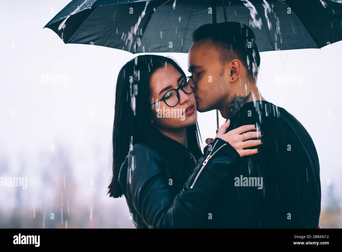 young couple standing under a dark umbrella Stock Photo - Alamy