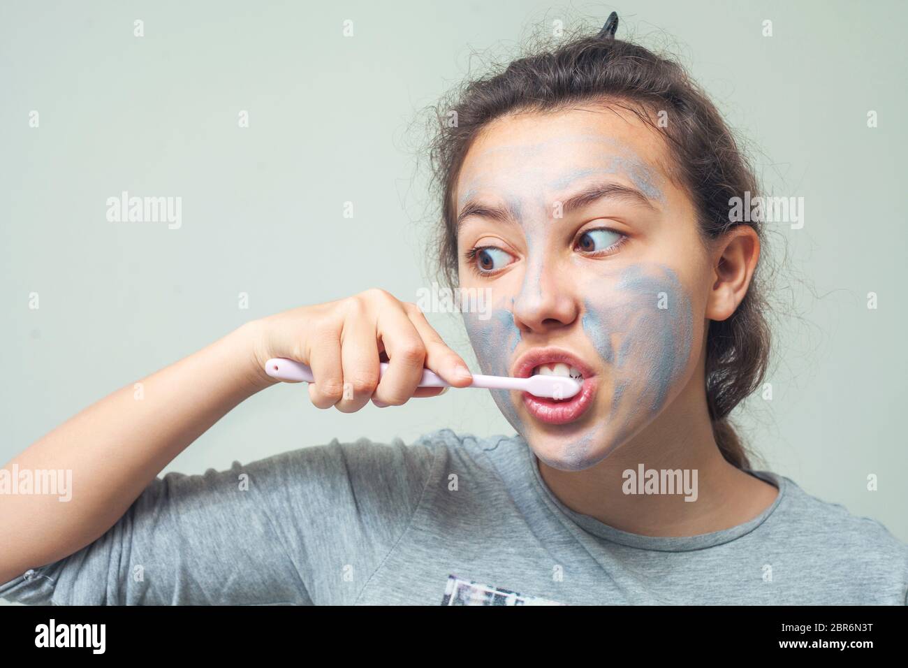 A teenage girl with a cosmetic mask on her face brushes her teeth. Facial scrub mask. The concept of health and beauty. Stock Photo