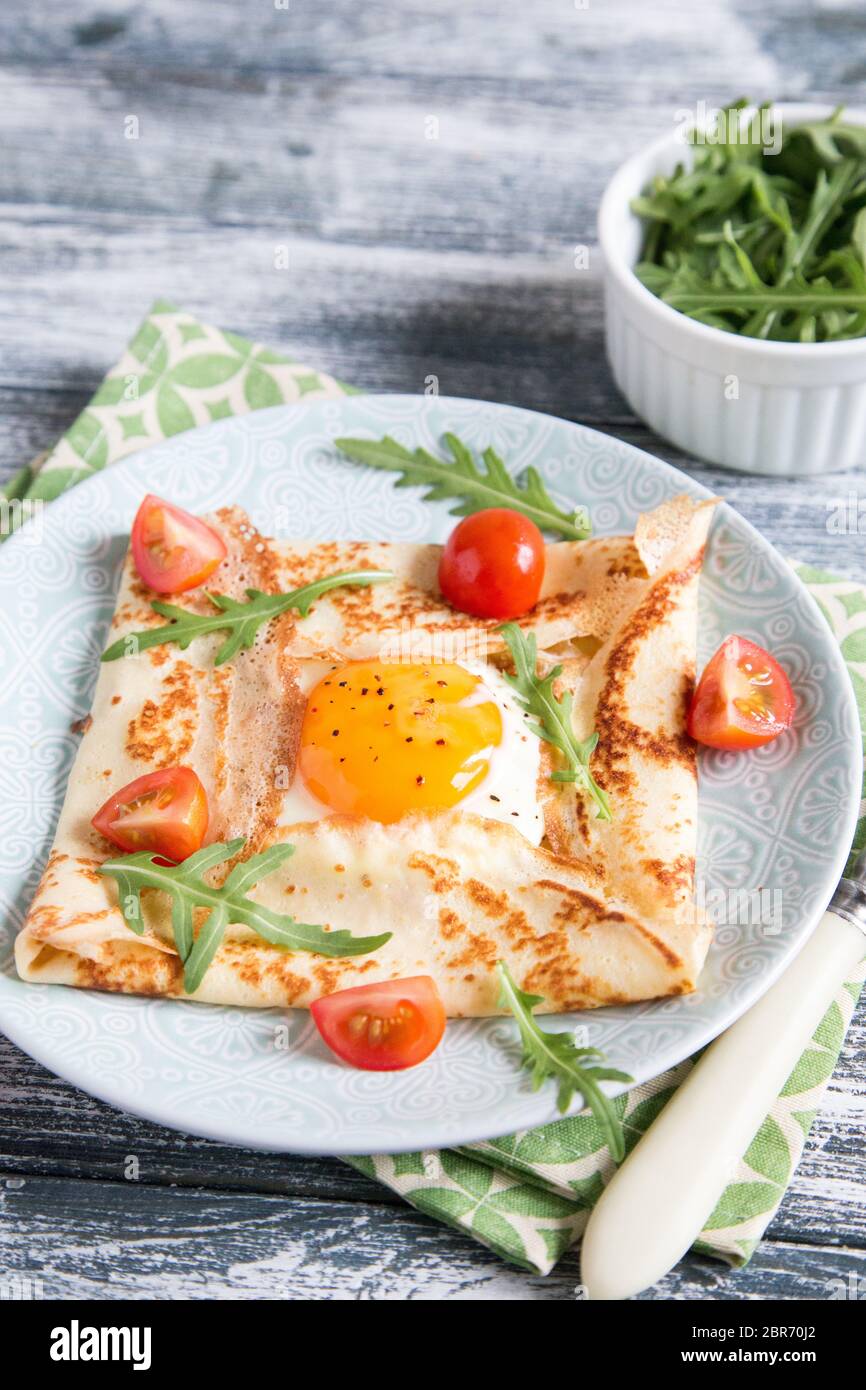 Crepes with eggs, cheese, arugula leaves and tomatoes.Galette complete. Traditional dish galette sarrasin Stock Photo