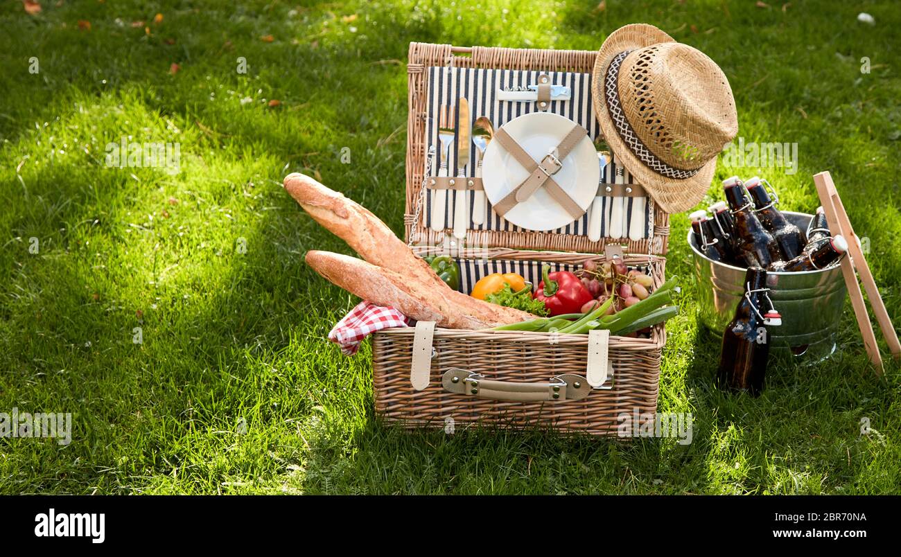 Picnic basket filled with several foodstuffs including baguettes and vegetables next to bucket of bottles Stock Photo