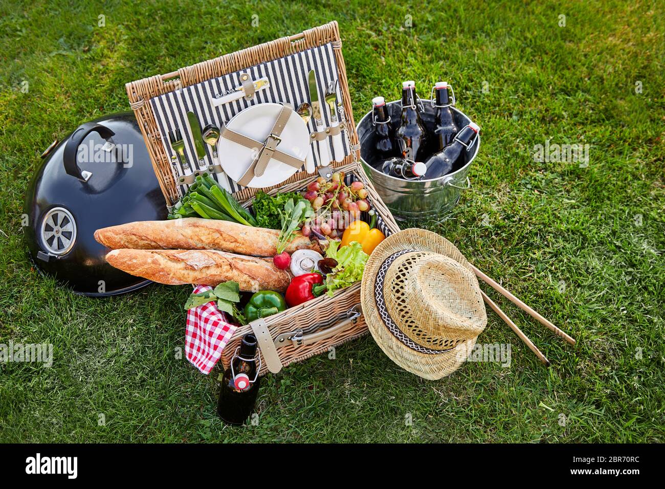 Vintage style wicker picnic hamper with an assortment of fresh vegetables for salads and crusty French baguettes alongside a silver cooler with bottle Stock Photo