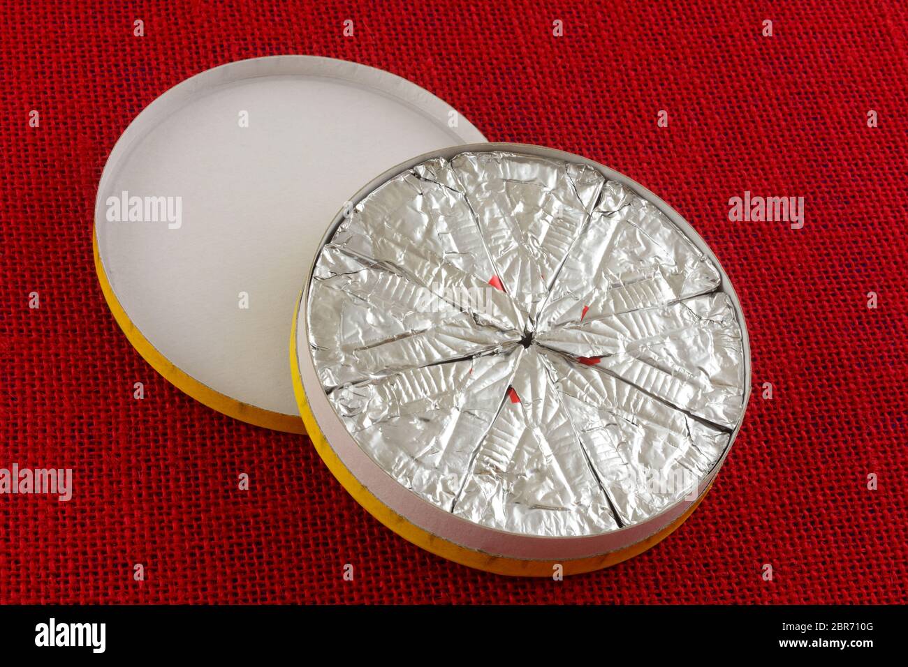 Wheel of individually sliced mini slices of brie cheese in cardboard box on red tablecloth Stock Photo