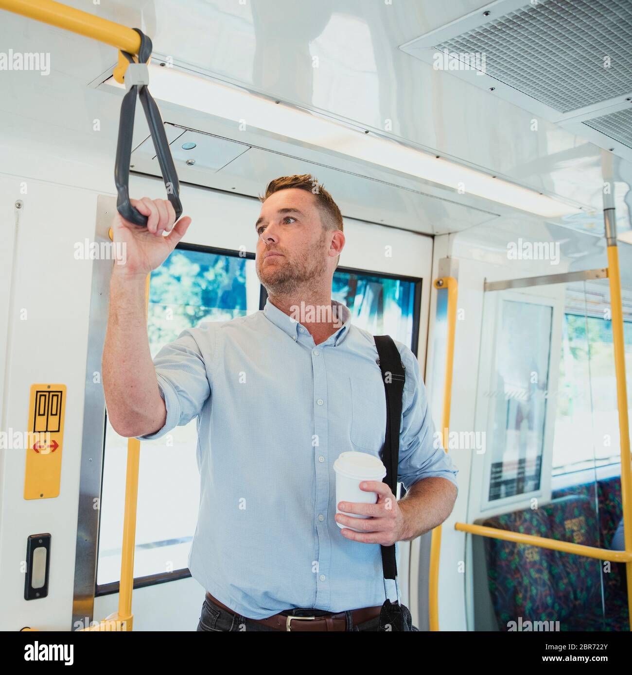 A side-view shot of a mid-adult businessman standing on a train commuting to work, he is holding a cup of coffee. Stock Photo