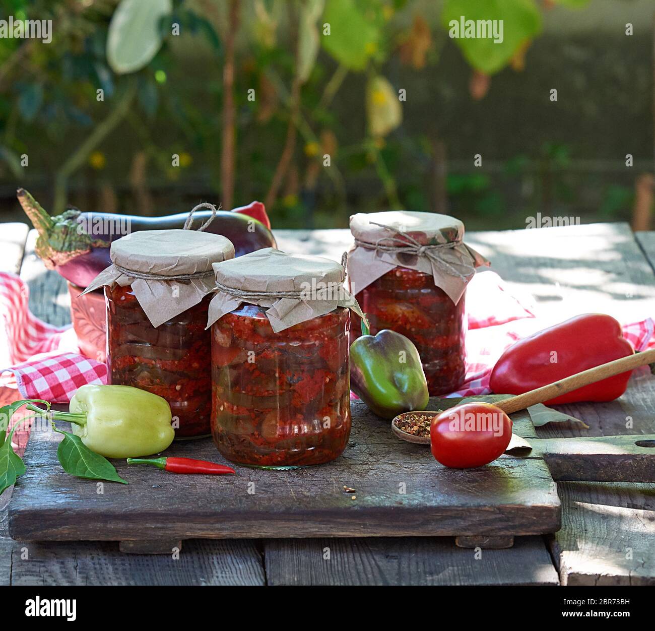 Canned eggplant slices in spicy vegetable sauce in glass jars on a wooden table Stock Photo