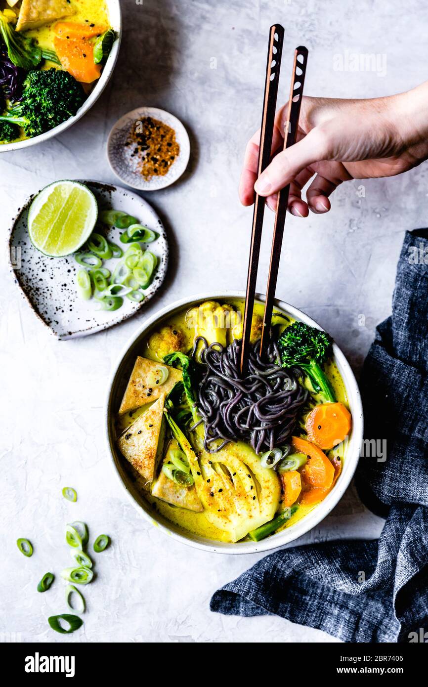 Thai curry with black rice noodles, tofu, carrot, broccolini, bok choy, cauliflower, lime, scallions Stock Photo