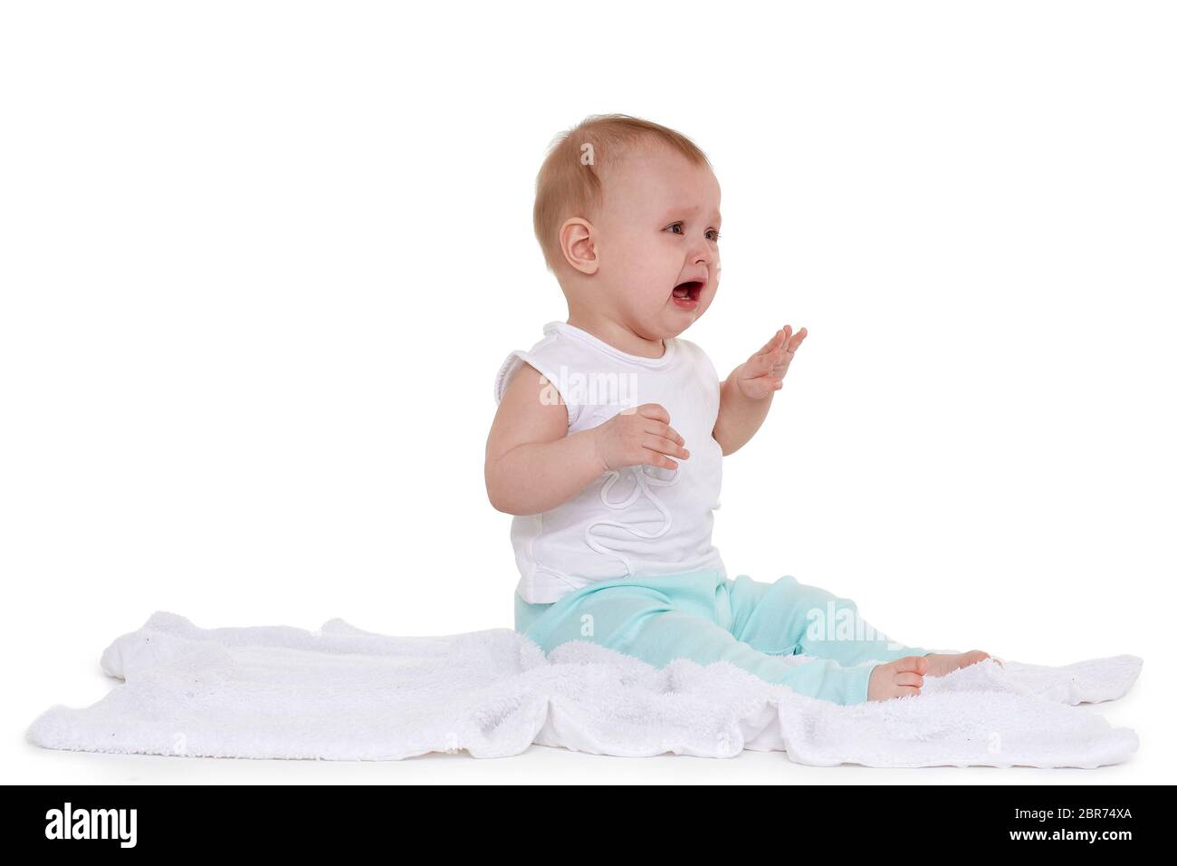 Little unhappy baby is sitting and crying on a plaid on white background. Eight months Stock Photo