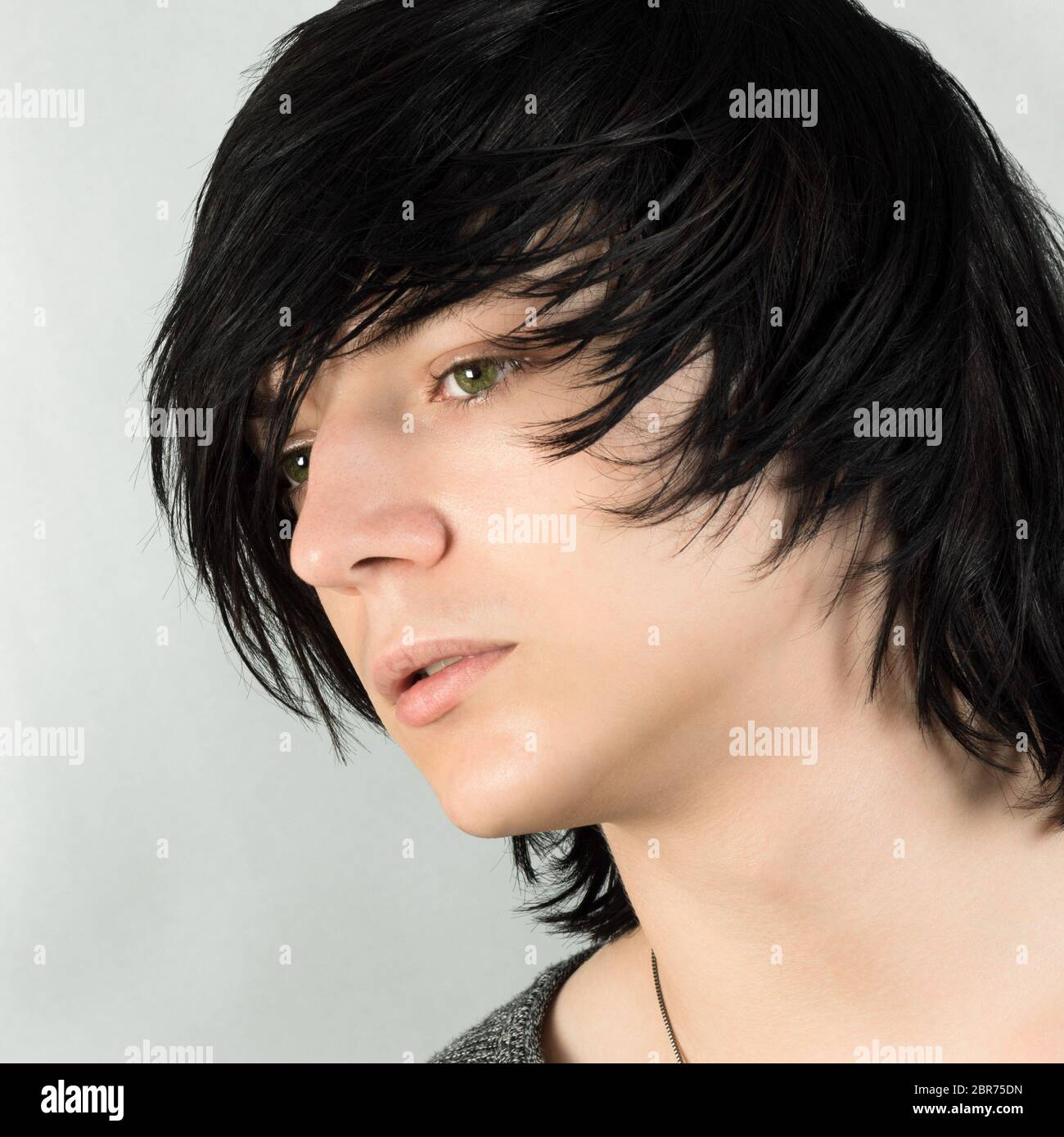 Close-up portrait of handsome teenage boy with black hair emo hairstyle on white background. Stock Photo