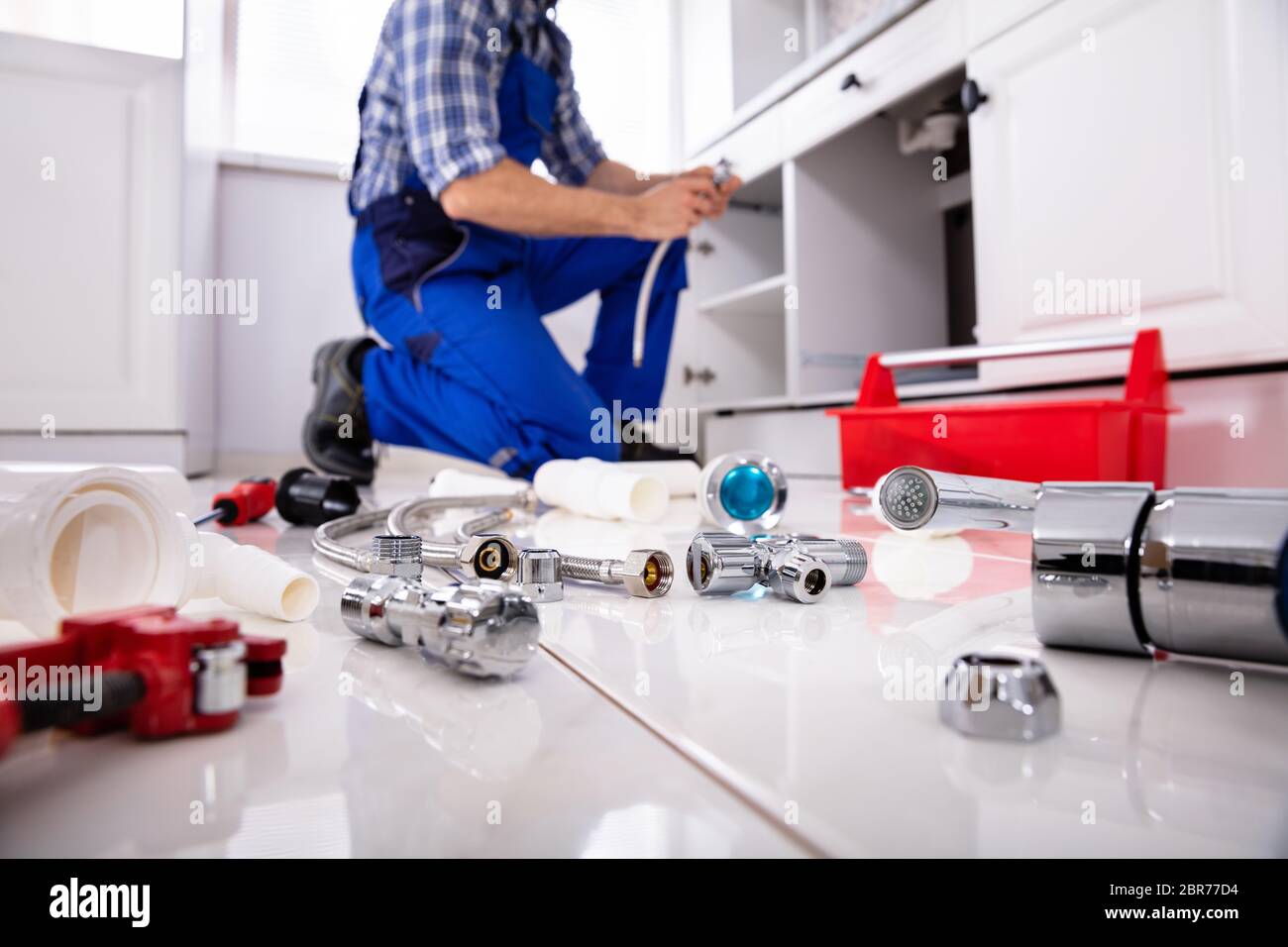 Plumber Tools And Equipment On Floor In Kitchen With Plumber Installing The Sink At Background Stock Photo