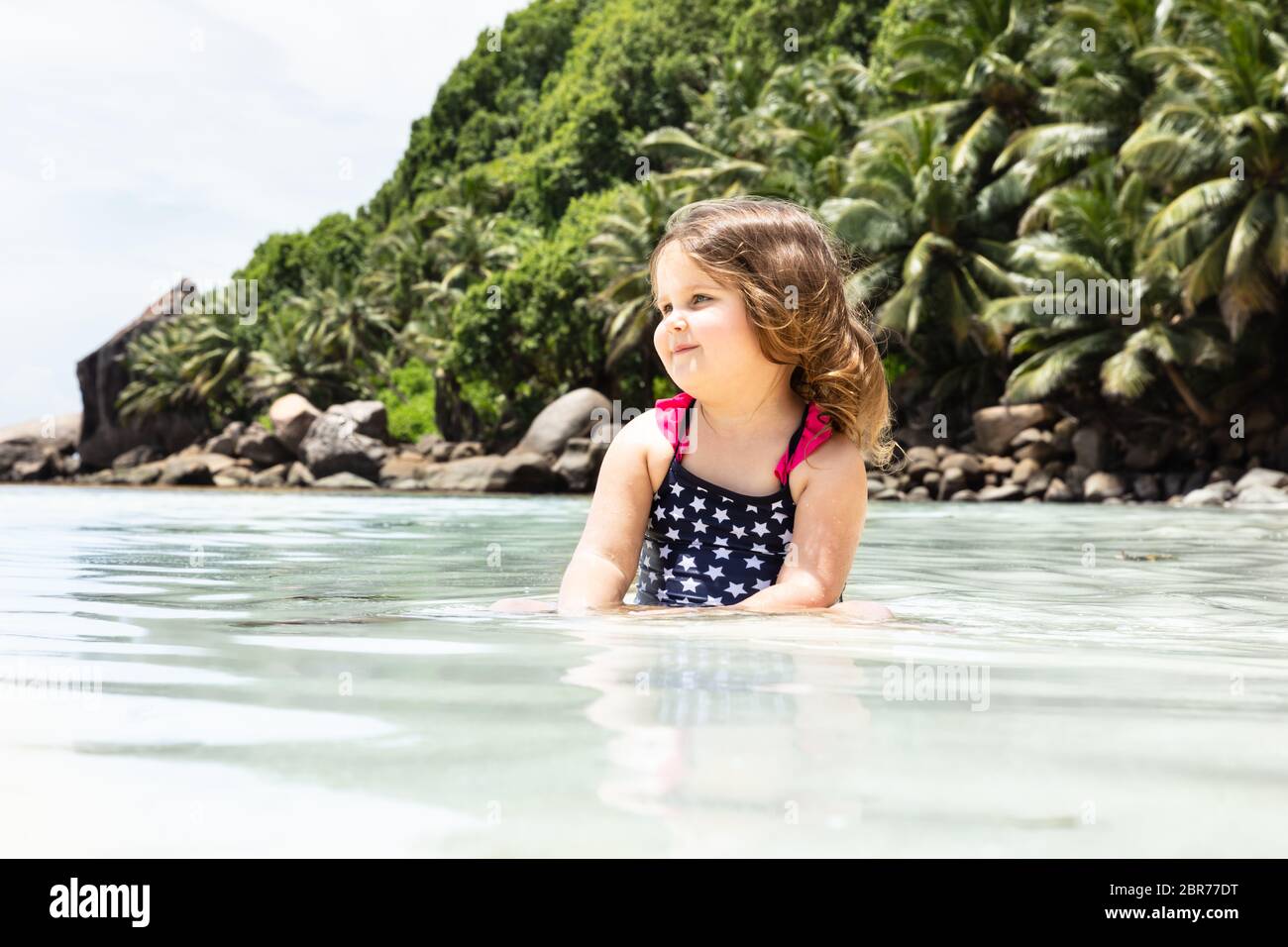 Portrait Of A Smiling Little Girl Sitting In The Shallow Water At Beach ...