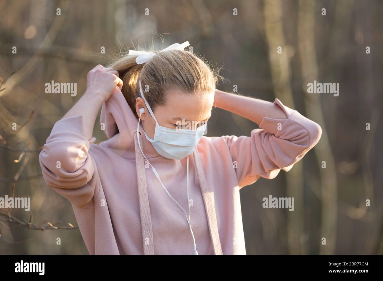 Portrait of caucasian sporty woman wearing medical protection face mask while walking in park, relaxing and listening to music. Corona virus, or Covid Stock Photo