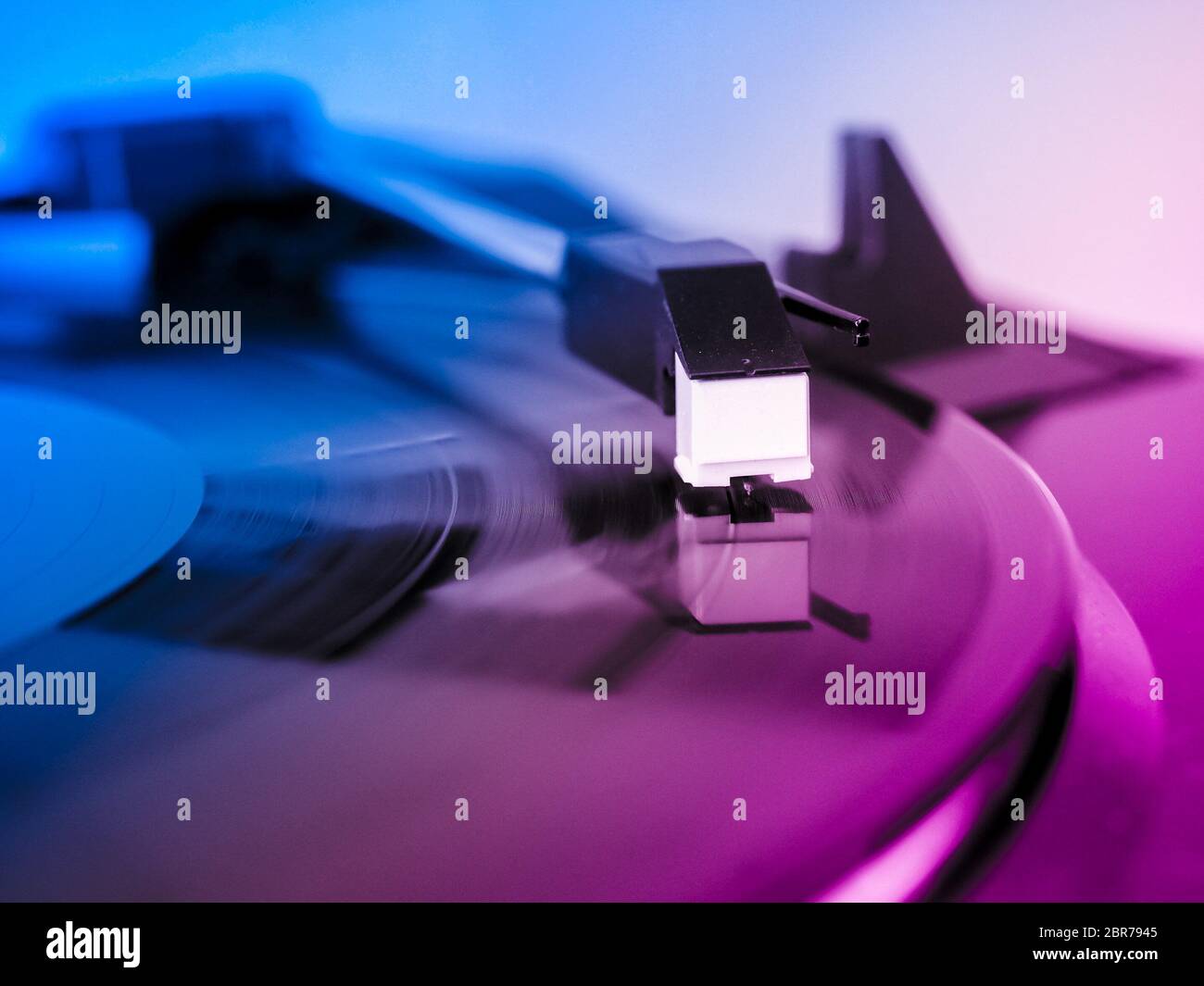 Vinyl record spinning on a turntable, focus on needle - pink and blue light Stock Photo