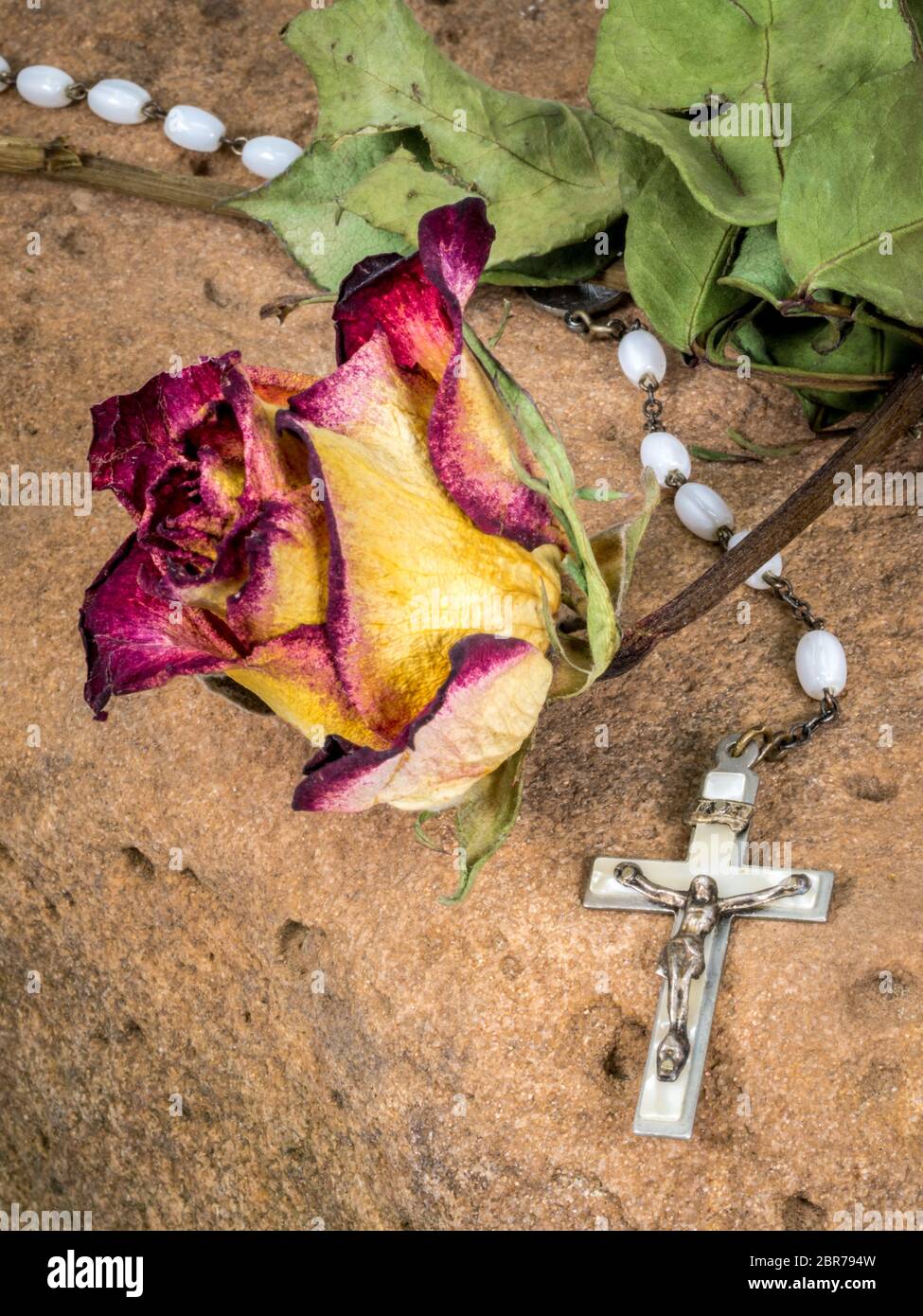Christian cross on rosary and a dry yellow red roses lie on a red ...