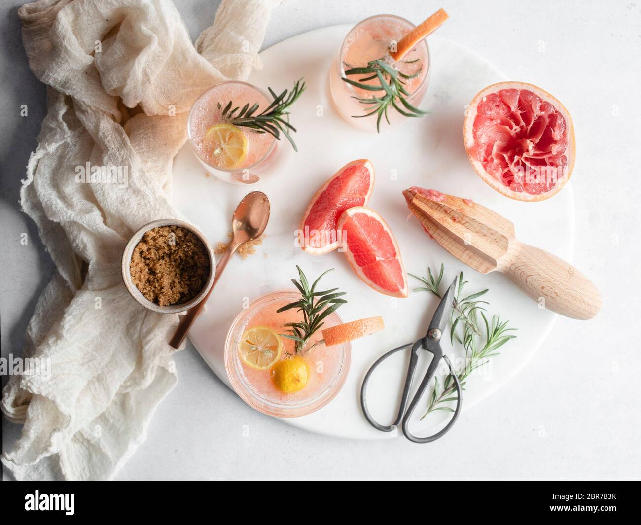 Overhead shot of 3 glasses of grapefruit cocktail on a round platter with rosemary and grapefruit slices and a cup of brown sugar with a rose gold spo Stock Photo