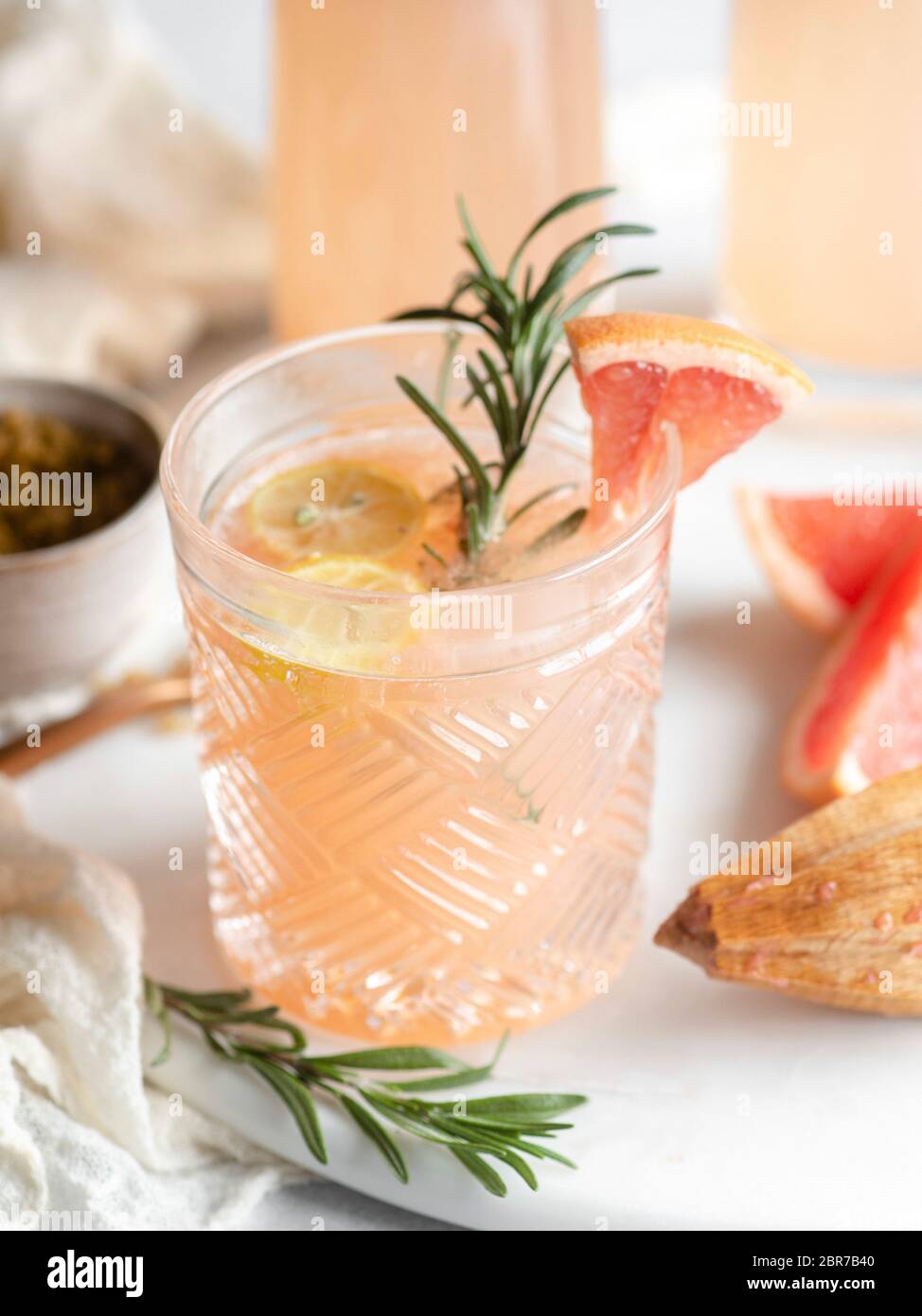 Old fashioned drinking glass filled with a grapefruit juice cocktail and garnished with lemon and rosemary on a blurred background Stock Photo