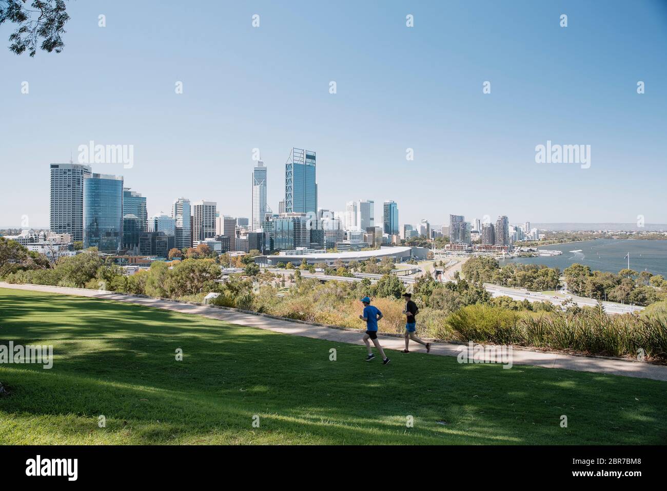 Two runners jogging through Kings Park in Peth with the cities sky line in the background. Stock Photo