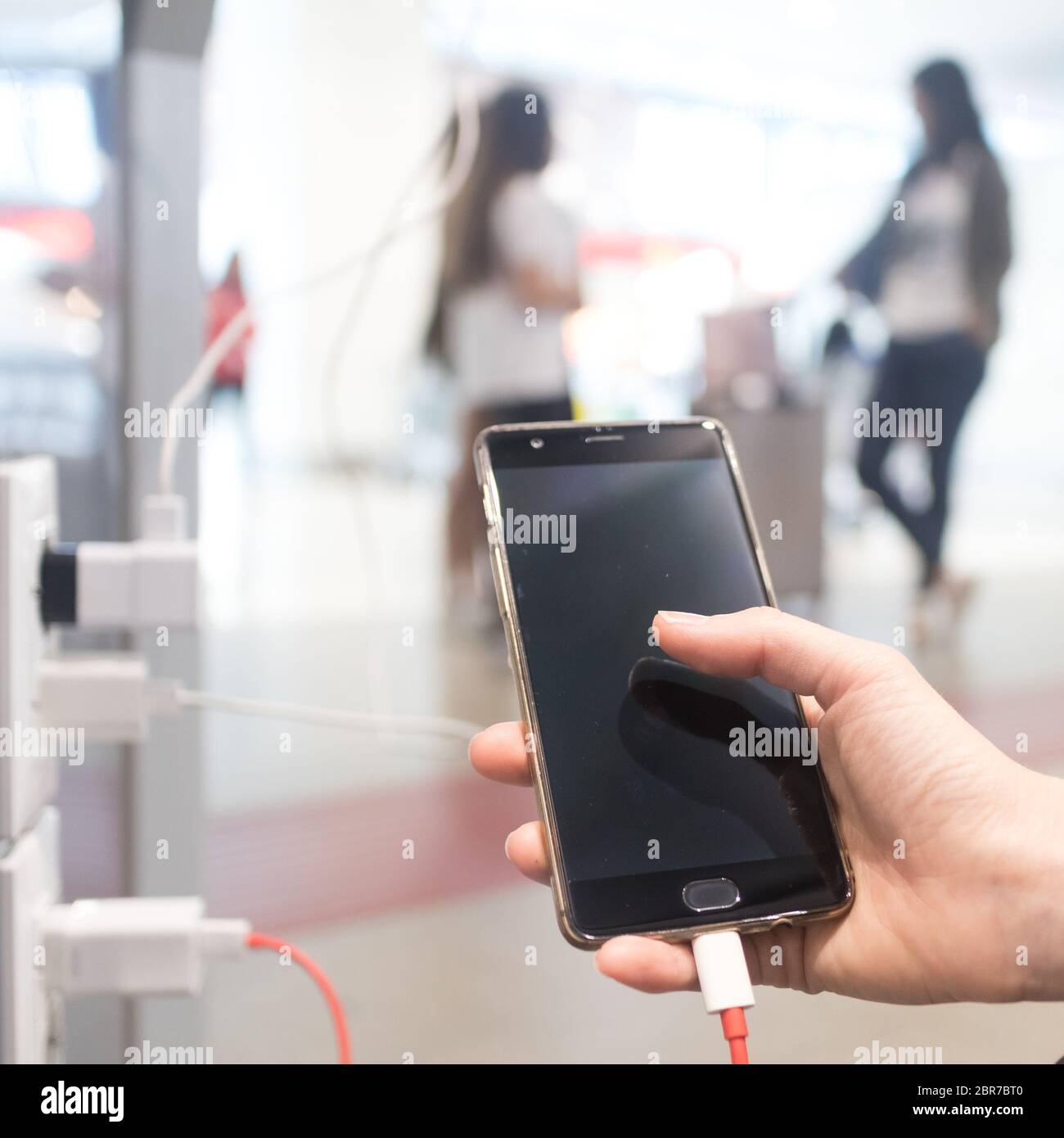 Female hands holding and using smartphone while charging it in a public