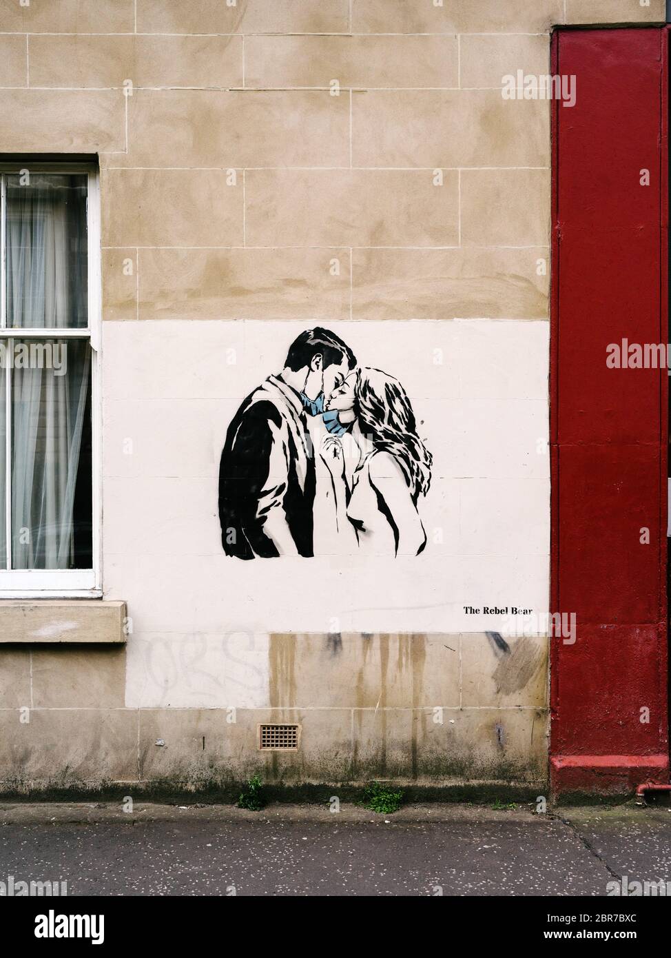 A new mural by street artist 'The Rebel Bear' showing a couple in an embrace and sharing a kiss with their surgical masks around their necks, highlighting social distancing guidelines and 'stay at home' advisories should be adhered to during the Coronavirus pandemic lockdown. Stock Photo