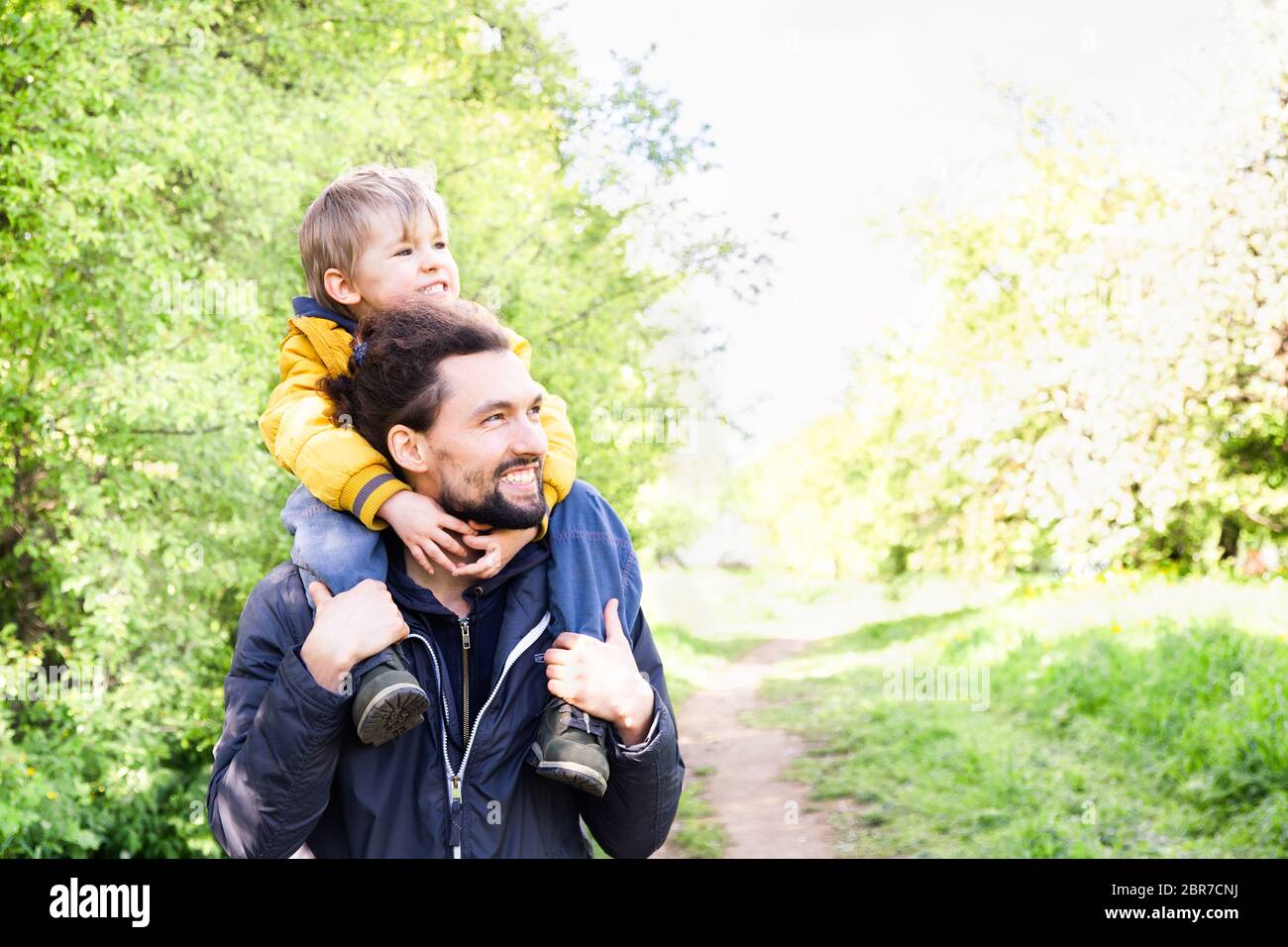 Happy family walk outdoor. Father riding his little son on his shoulders in a park. Fathers day and family fun concept Stock Photo