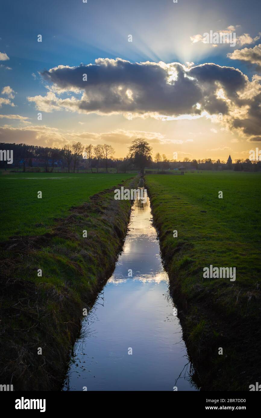 Sunset with water ditch between fields in the Lüneburg Heath, Northern Germany. Backlit photography. Sonnenuntergang mit Wassergraben zwischen Feldern Stock Photo