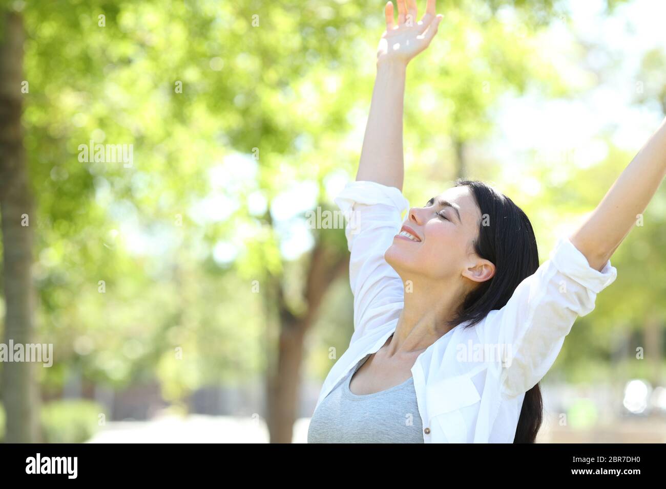 Happy adult woman celebrating new day raising arms in a park with a ...