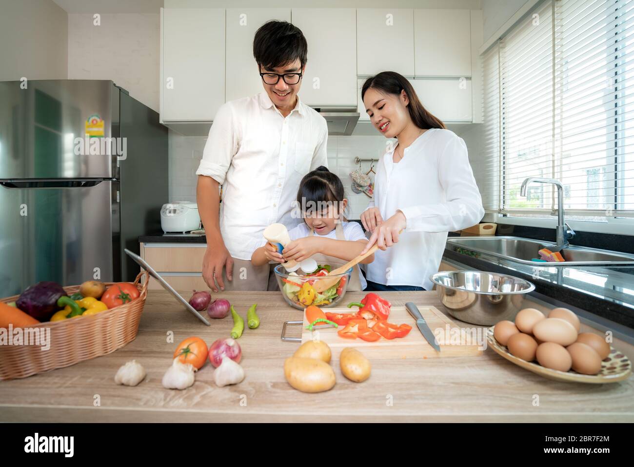 Asian family with father, mother and daughters preparing and cooking salad in the kitchen at home. Family life love relationship, or home fun leisure Stock Photo