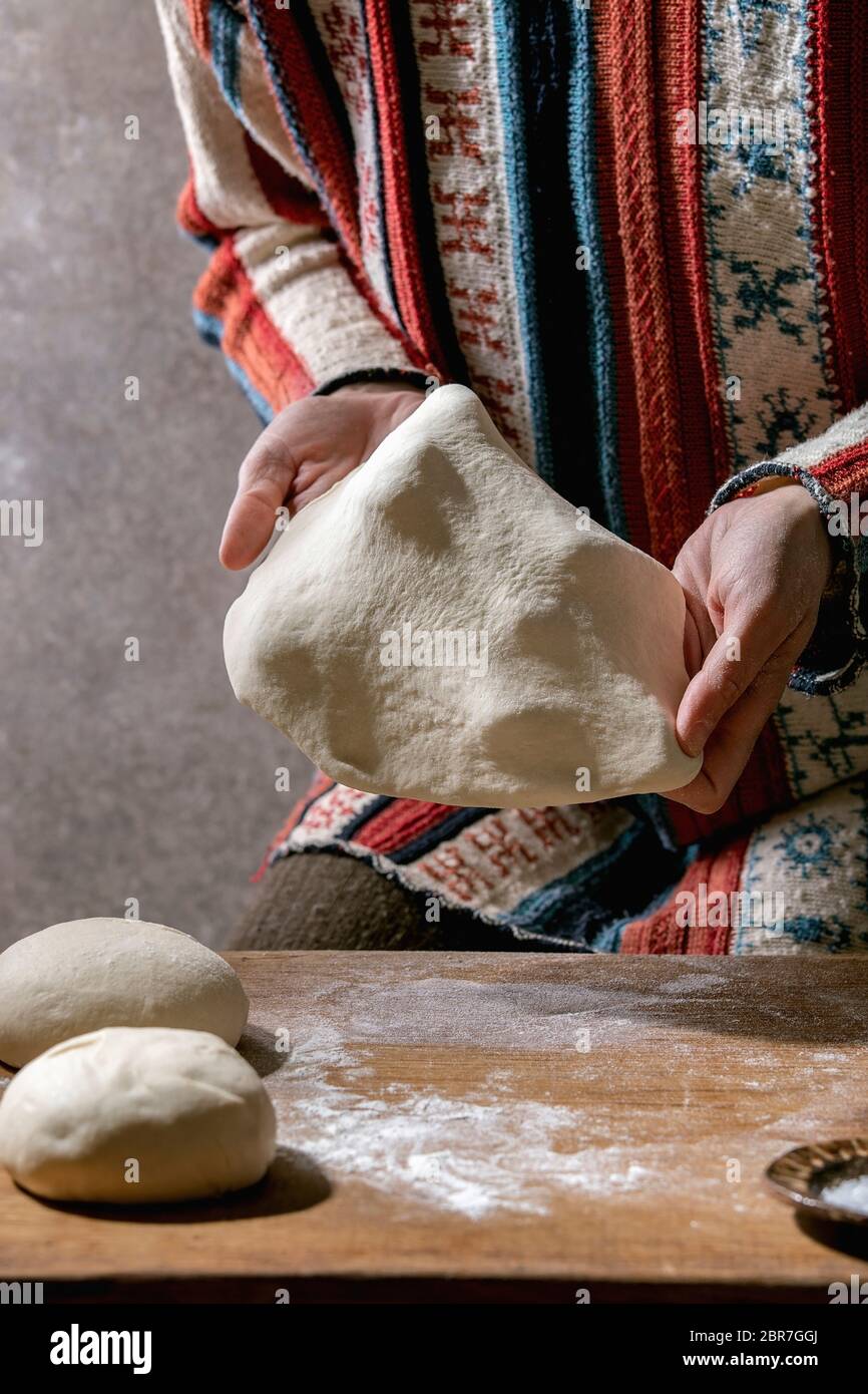 Woman in knitted sweater cooking italian pizza napolitana. Pulling fresh homemade wheat dough on wooden kitchen table. Home baking. Stock Photo