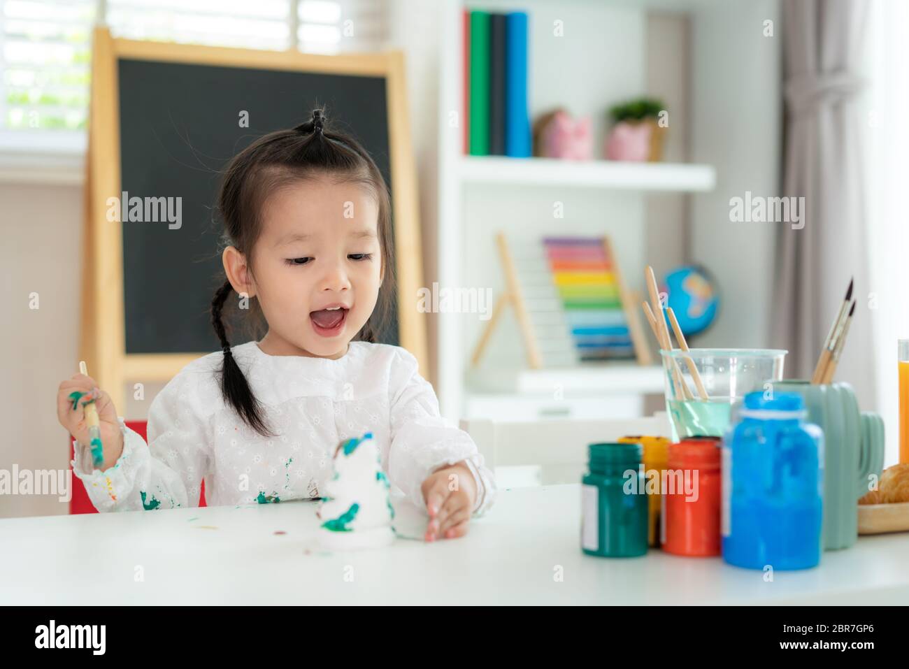 Asian kindergarten school girl looking happy and smile while painting Plaster doll with Acrylic water color paint in living room at home. Homeschoolin Stock Photo