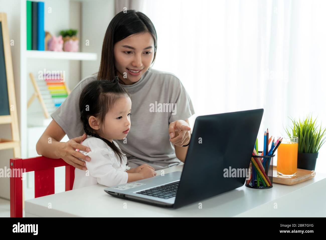 Asian kindergarten school girl  with mother video conference e-learning with teacher on laptop in living room at home. Homeschooling and distance lear Stock Photo