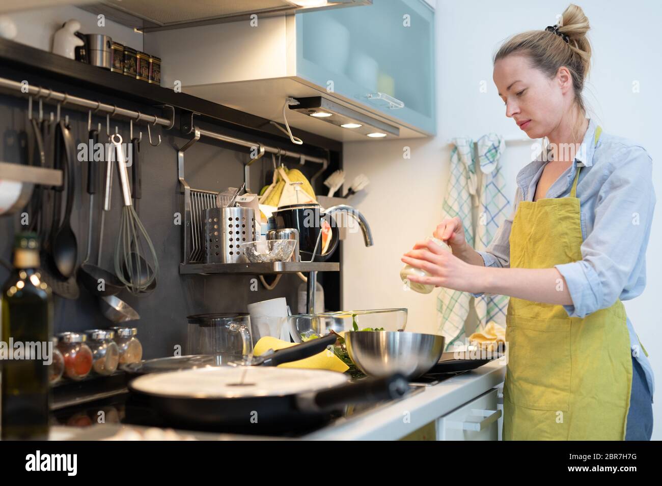 Stay at home housewife woman cooking in kitchen, stir frying dish in a