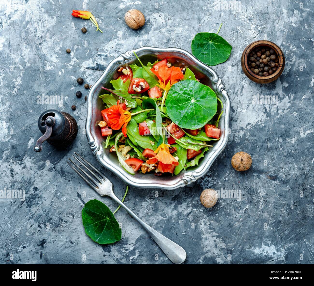 Healthy salad with flowers, nasturtium leaves, tomatoes and nuts. Summer food. Stock Photo