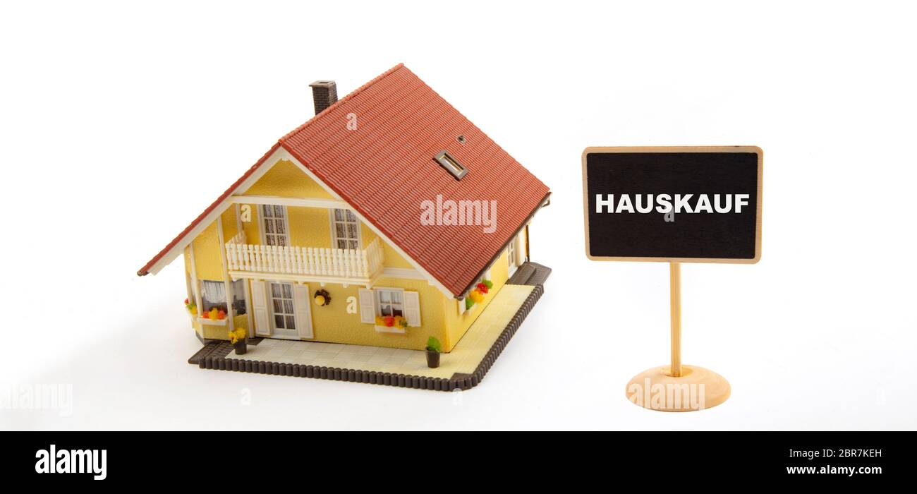 Concept Hauskauf means House purchase. Business Real Estate with Toy House and little Blackboard Sign on white Background Stock Photo