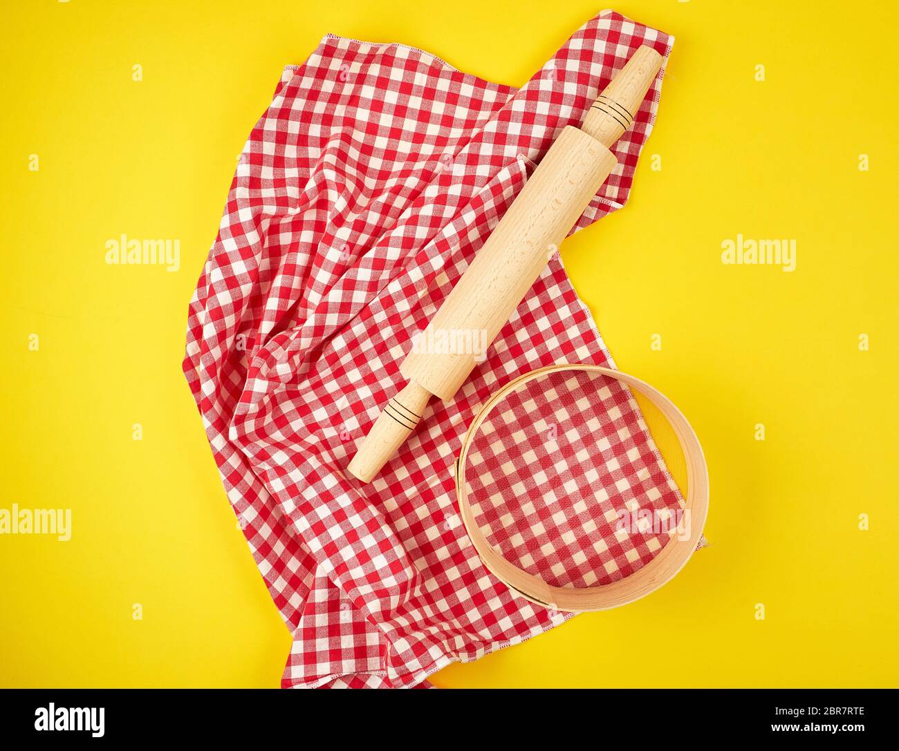 new wooden rolling pin on a red textile napkin and a round sieve for