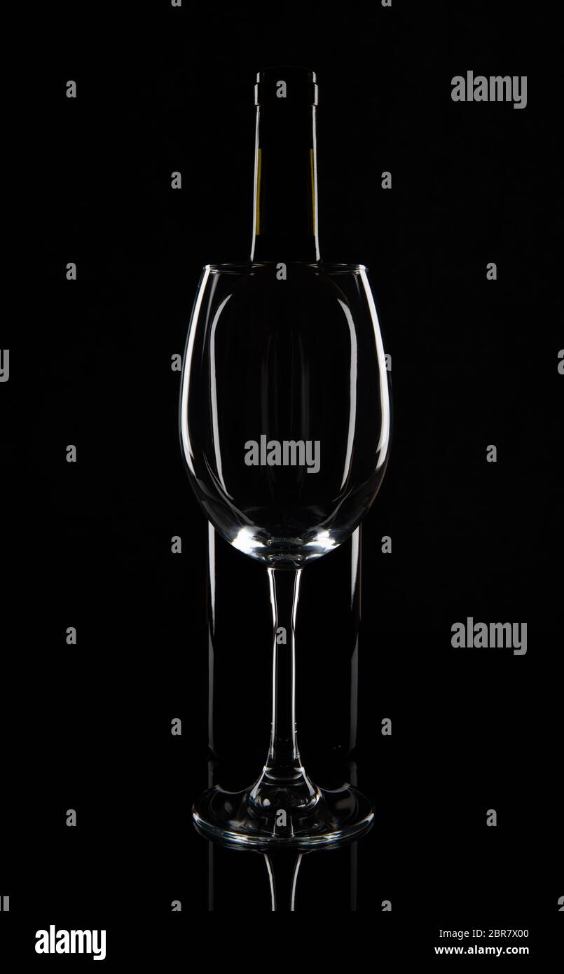 Empty wine glass in front of the wine bottle, isolated on black background. Stock Photo