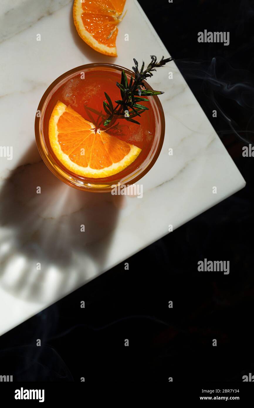 Negroni cocktail with a slice of orange and a smoking rosemary sprig garnish. The view is overhead looking down onto a marble tabletop with a slice of Stock Photo