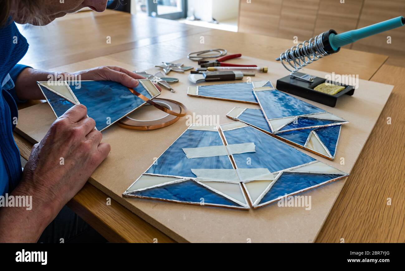 Woman working on hobby craft stained glass panels for lamp shade with tools, Scotland, UK Stock Photo