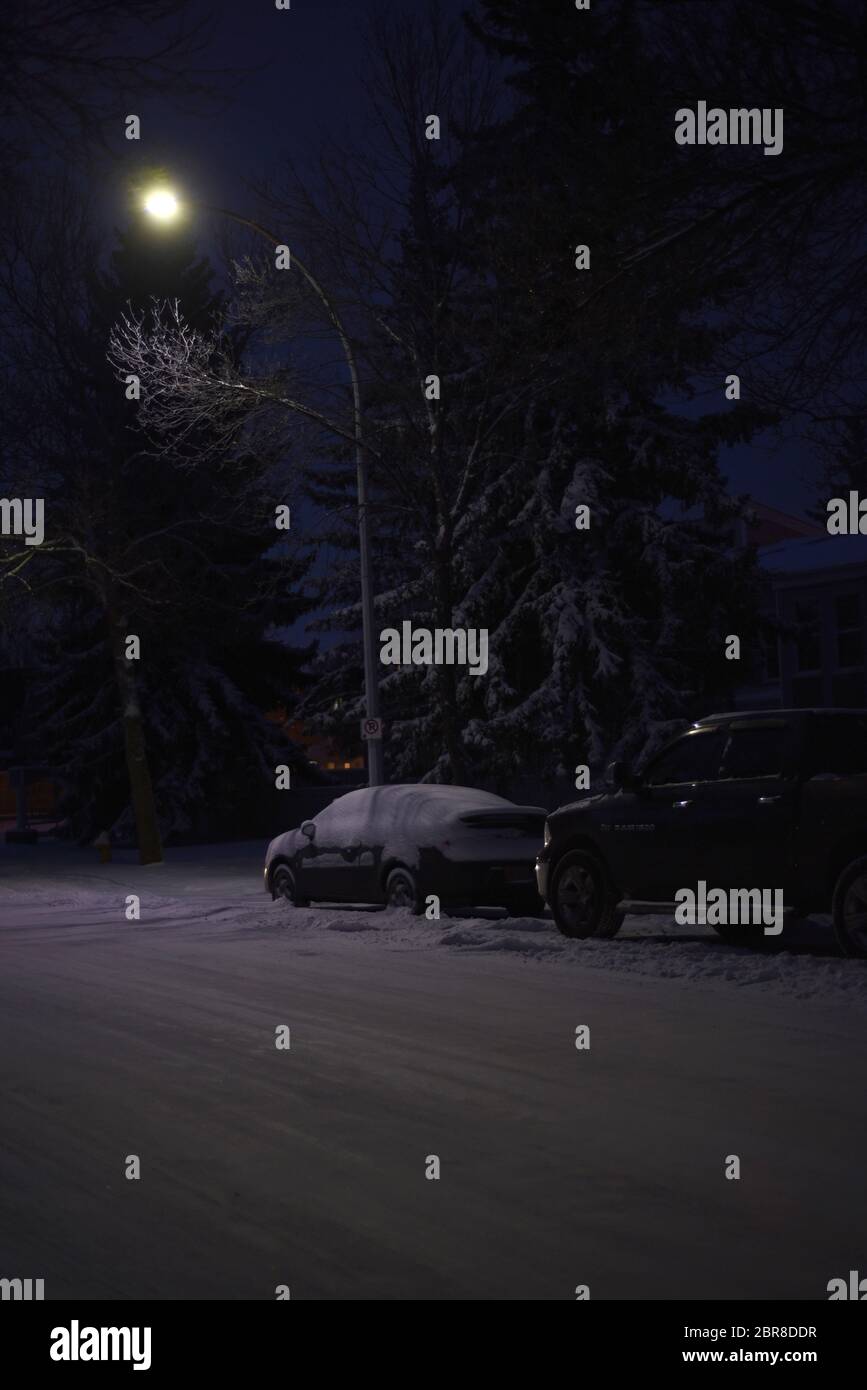 Snow covered vehicles on an icy snowy road under a street light at night in Edmonton, Alberta, Canada Stock Photo