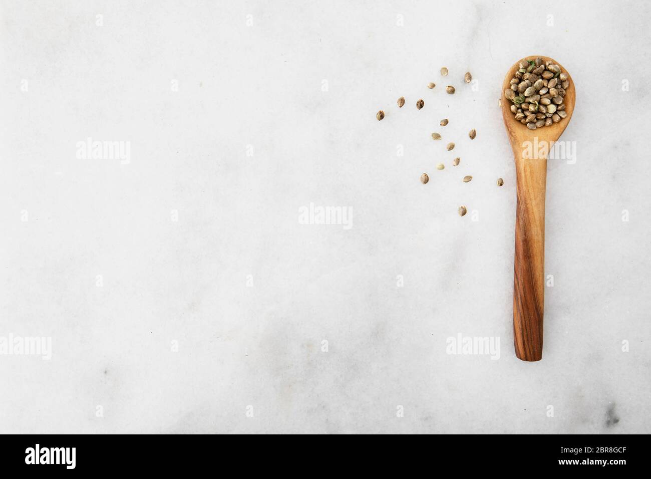 Cannabis seeds in a wooden spooon on a light marble surface with copy space, viewed from directly above. Stock Photo