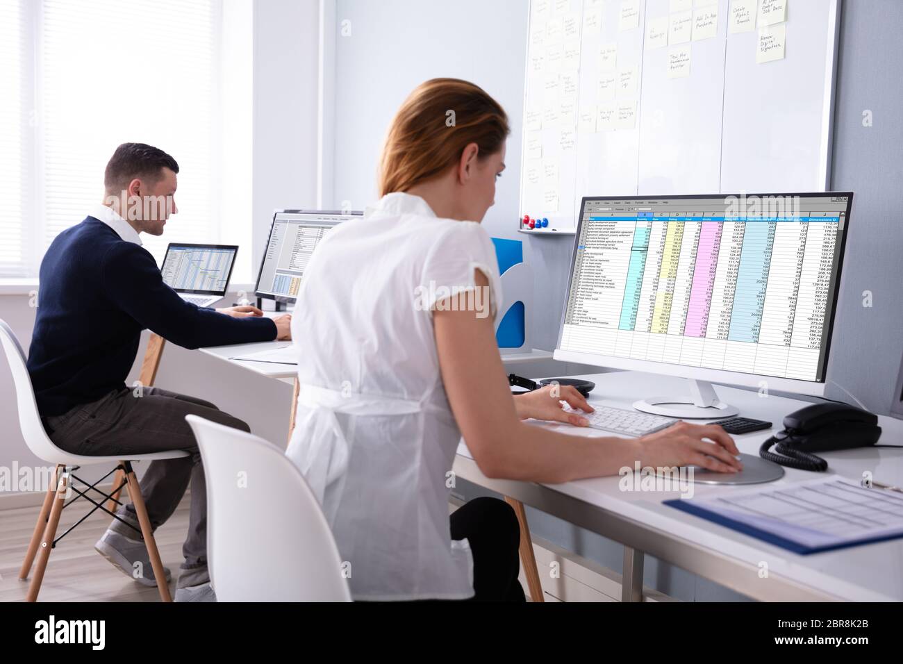 Side View Of Male And Female Businesspeople Sitting In Office Examining Report On Computer Stock Photo